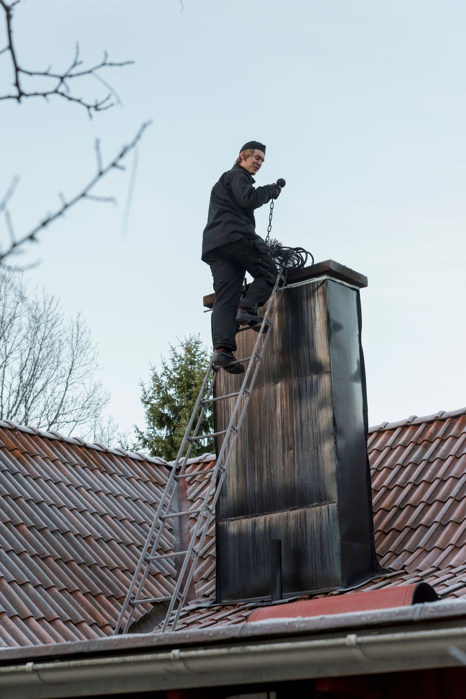 A professional chimney sweep on a ladder servicing a residential rooftop chimney
