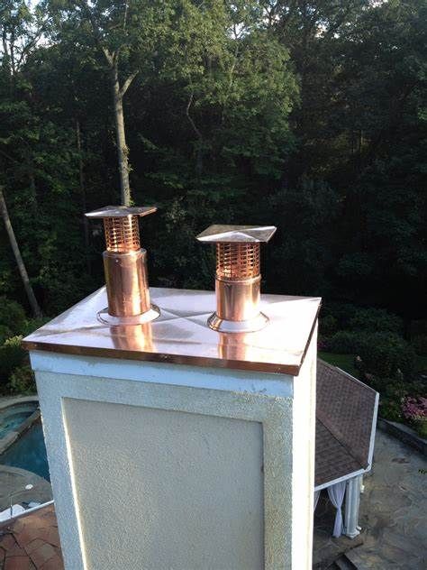 Copper-topped chimney with two copper chimney caps against a backdrop of trees.
