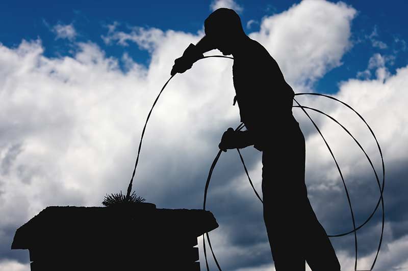 Silhouette of a person cleaning a chimney against a cloudy sky.