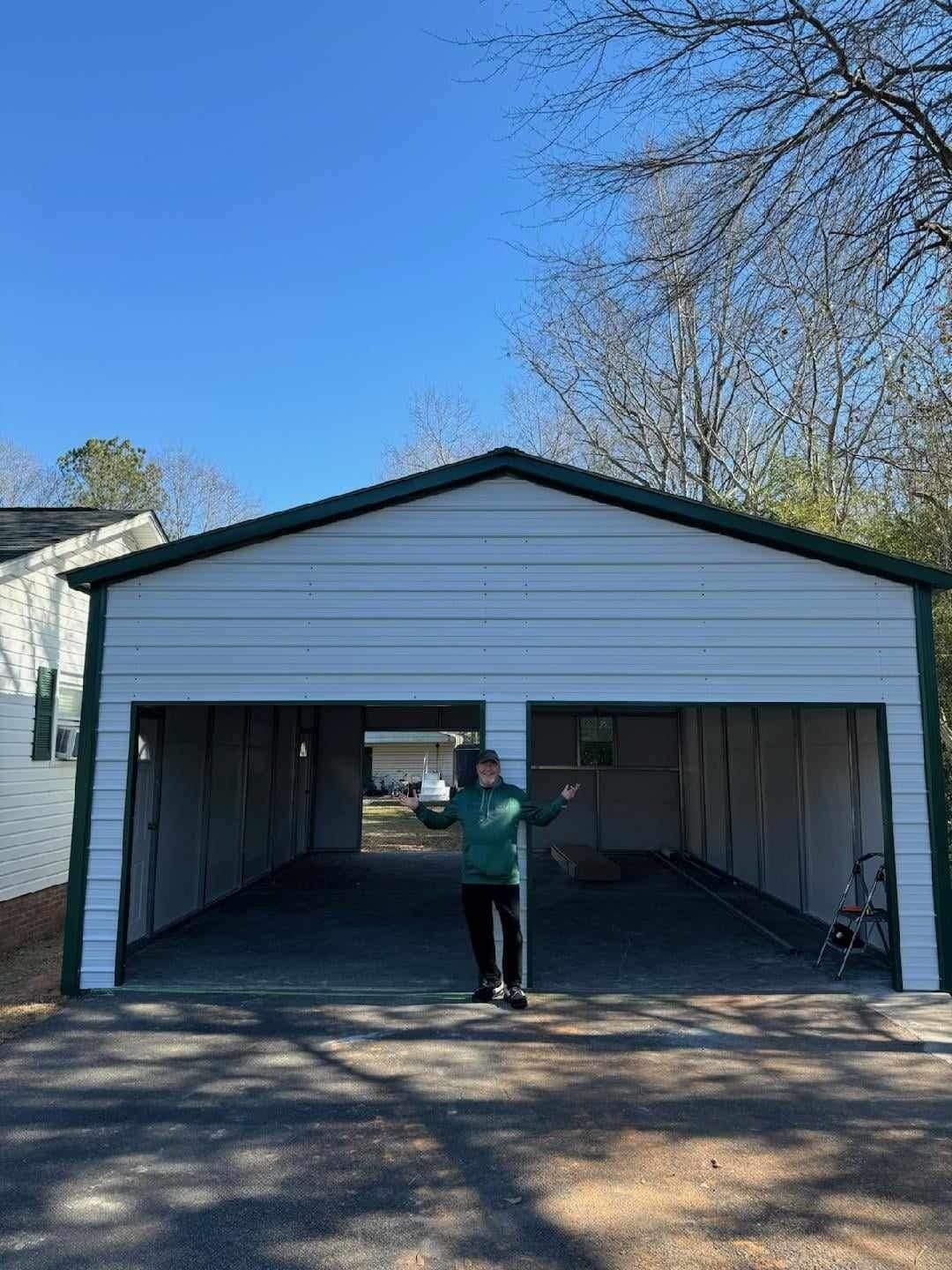 Person standing in front of an open white double garage on a sunny day