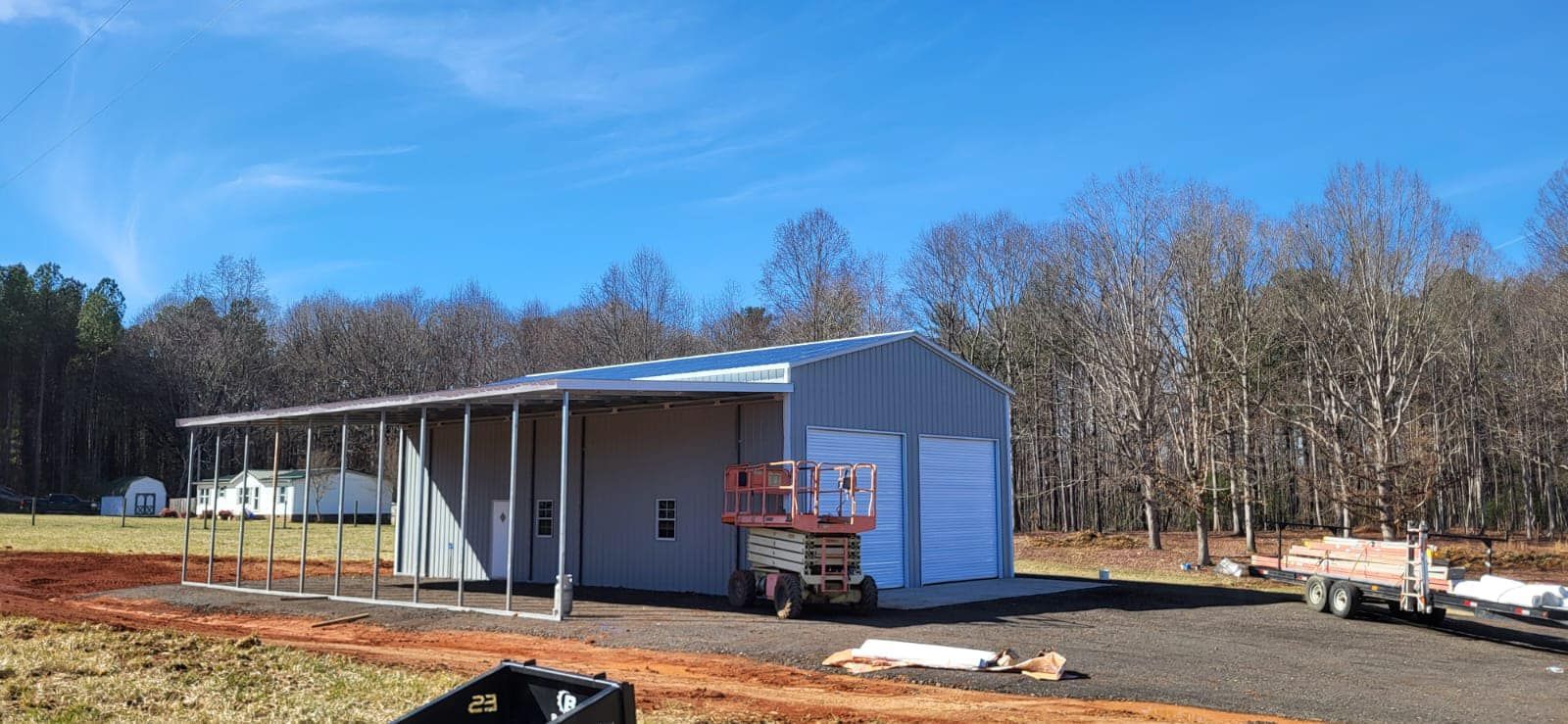Small gray metal building under construction with scaffolding and trees in the background