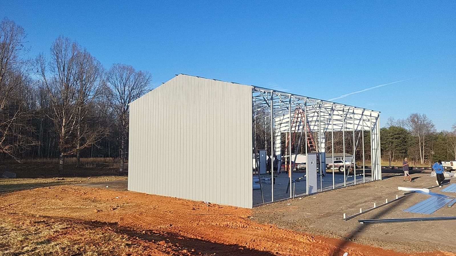 Partially built metal frame structure with white exterior walls on a dirt lot under a clear blue sky
