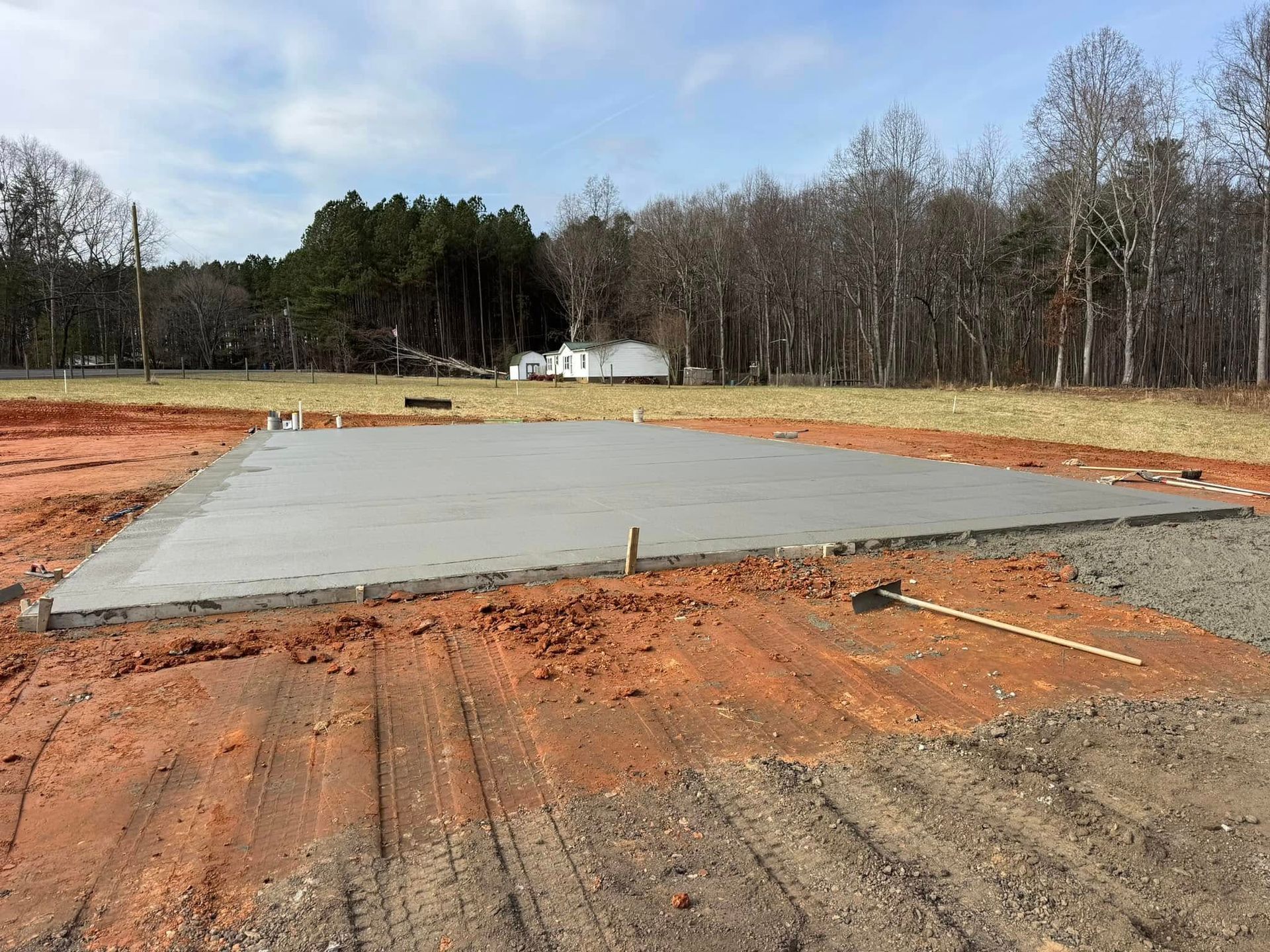 Concrete slab on a cleared dirt lot with trees and a blue sky in the background