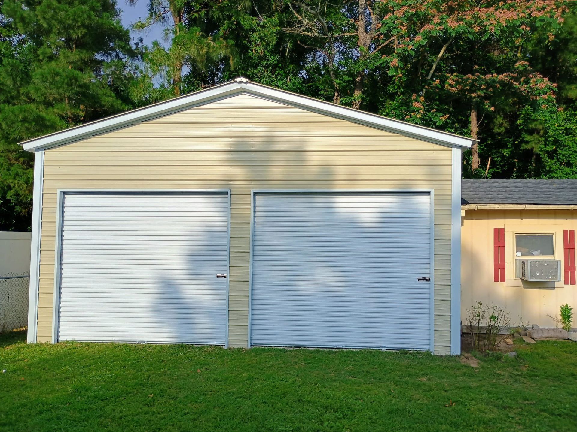 White double garage doors on a beige detached garage in a grassy yard with trees behind.