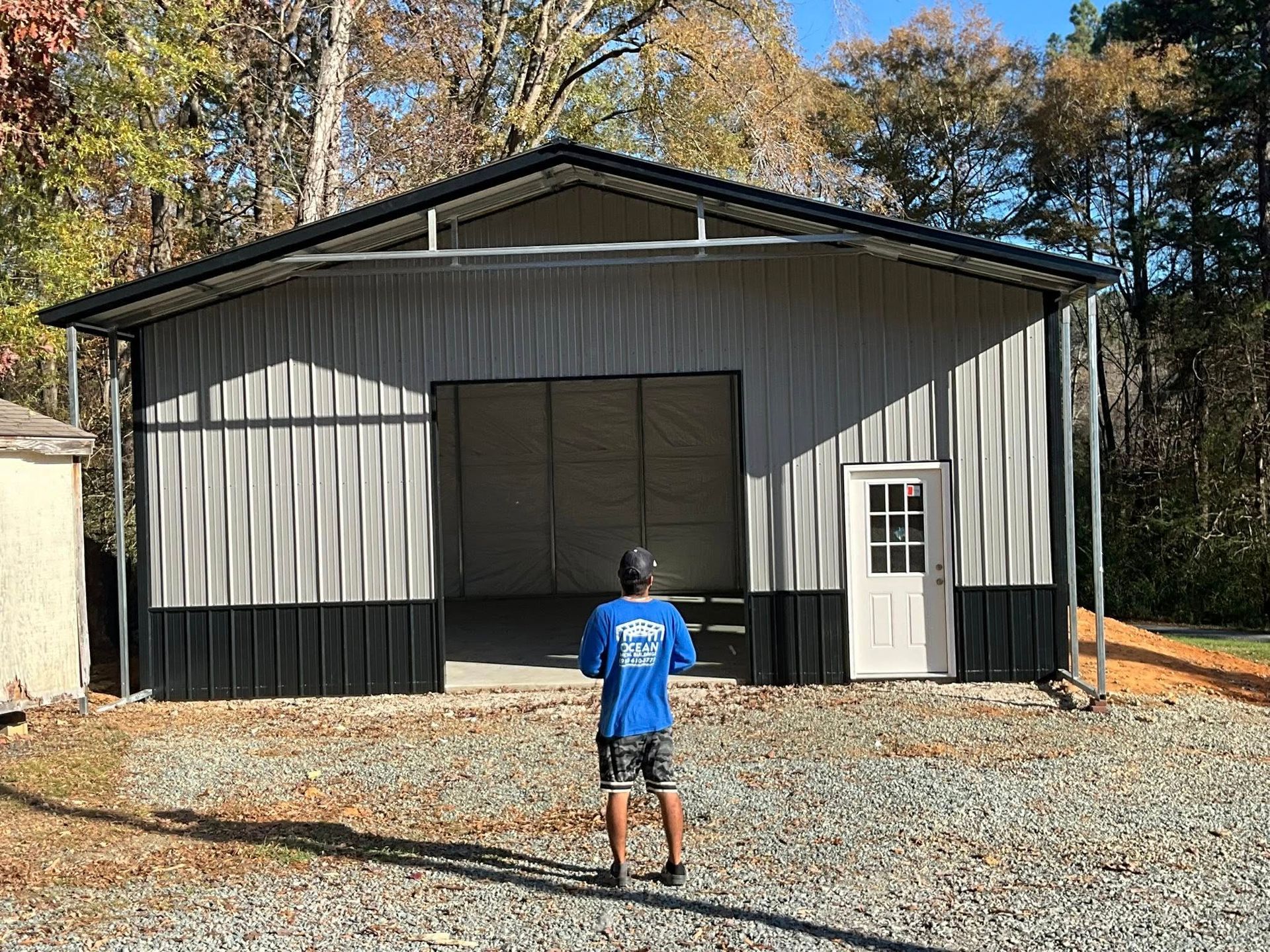 Large metal building with open doors and a person standing in front on gravel.