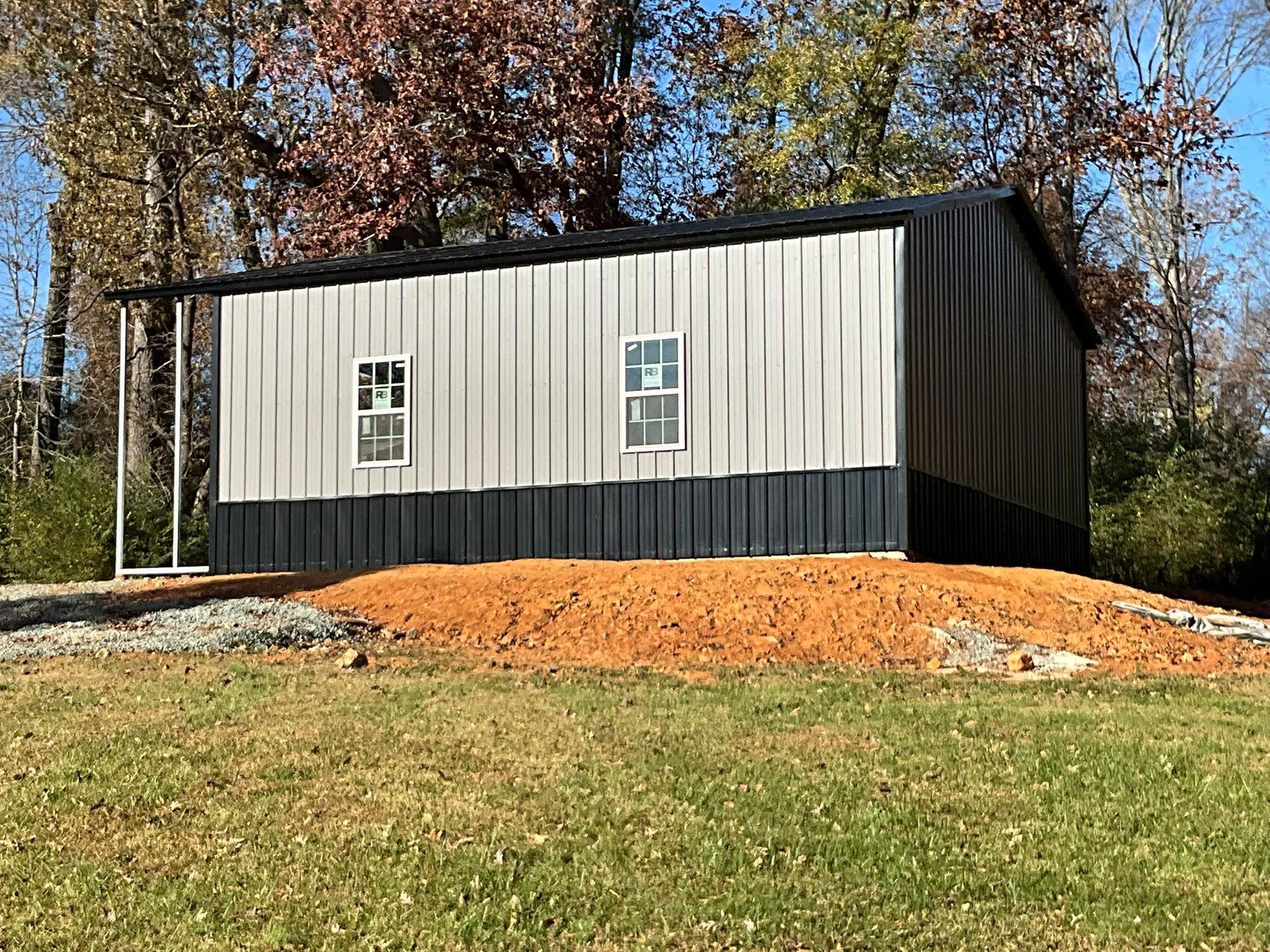 Small gray-and-black shed on a grassy hill with autumn trees in the background