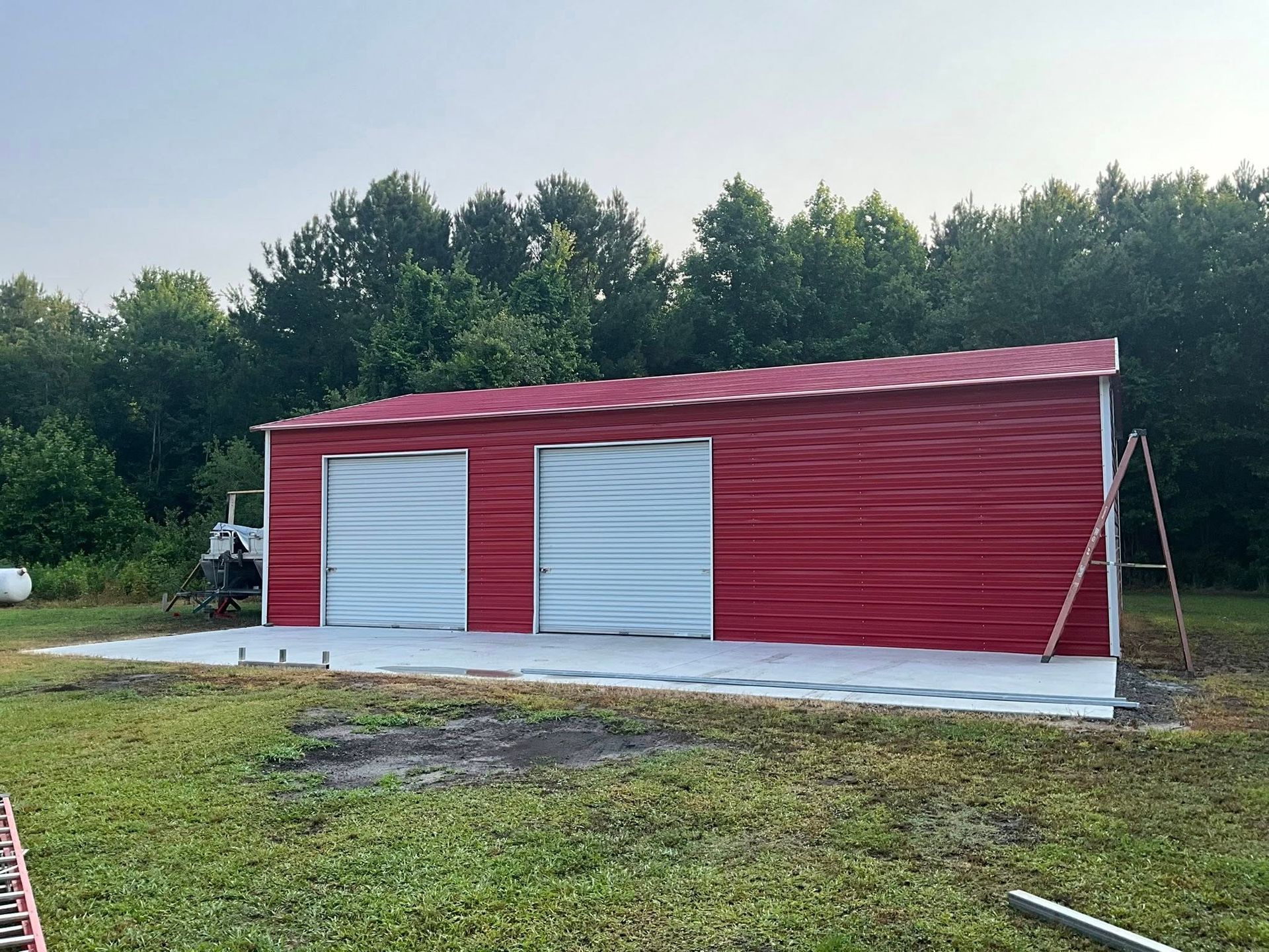 Red metal storage shed with two white doors on a concrete slab in a grassy yard.