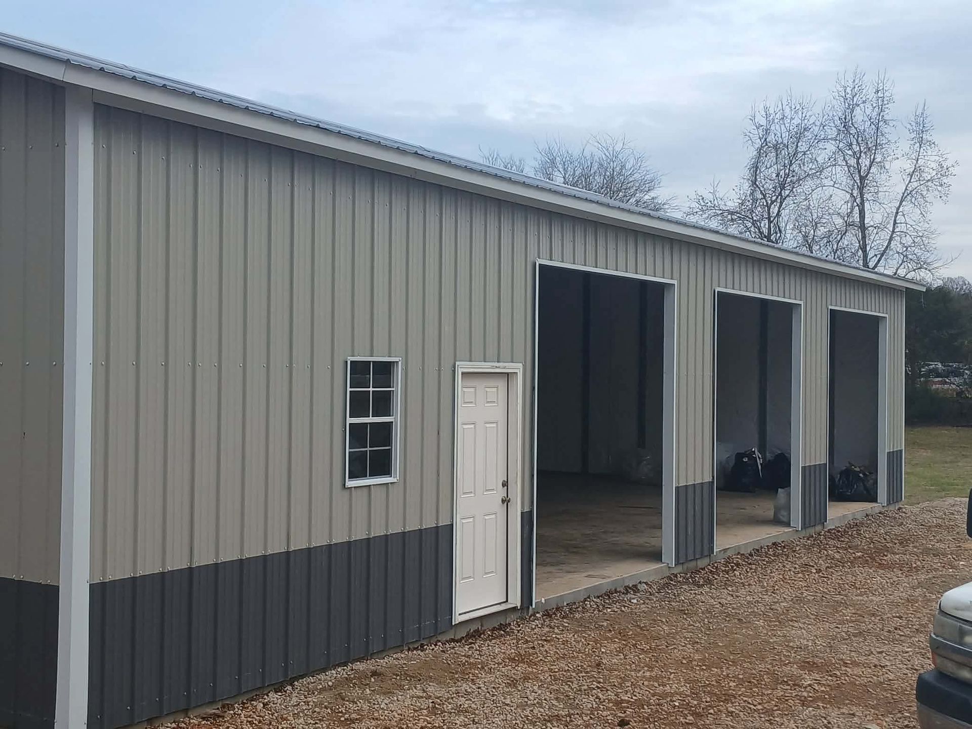 Tan-and-dark gray metal storage building with large open garage bays and a side door