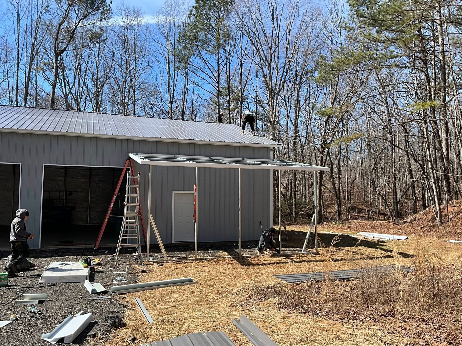 Person on ladder beside gray shed under construction in a wooded yard