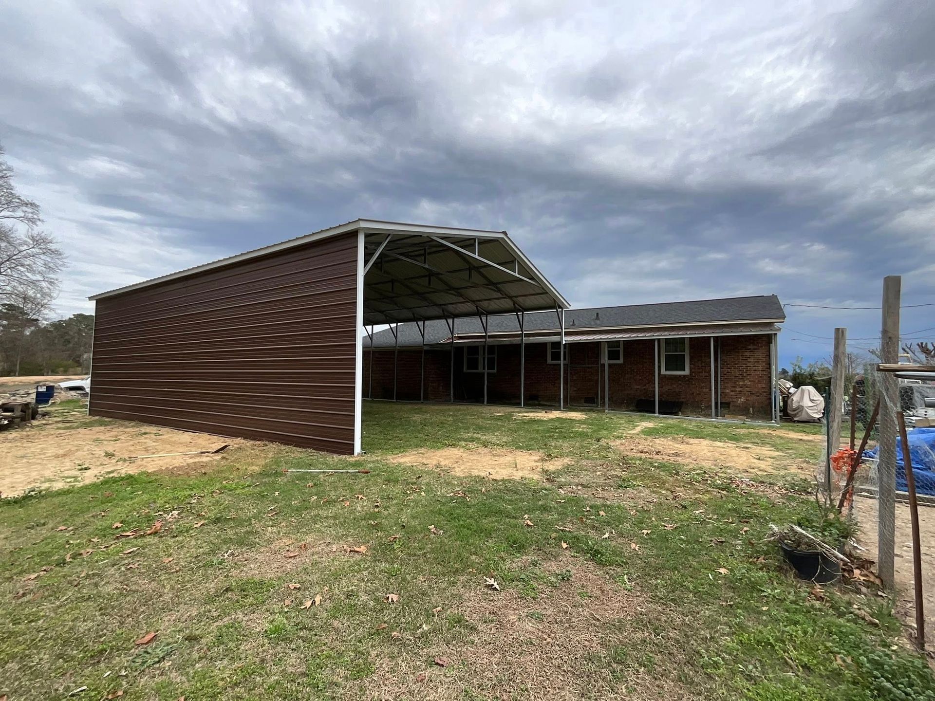 Rustic barn-like building with brown siding and a metal roof under a cloudy sky, set in a grassy field.
