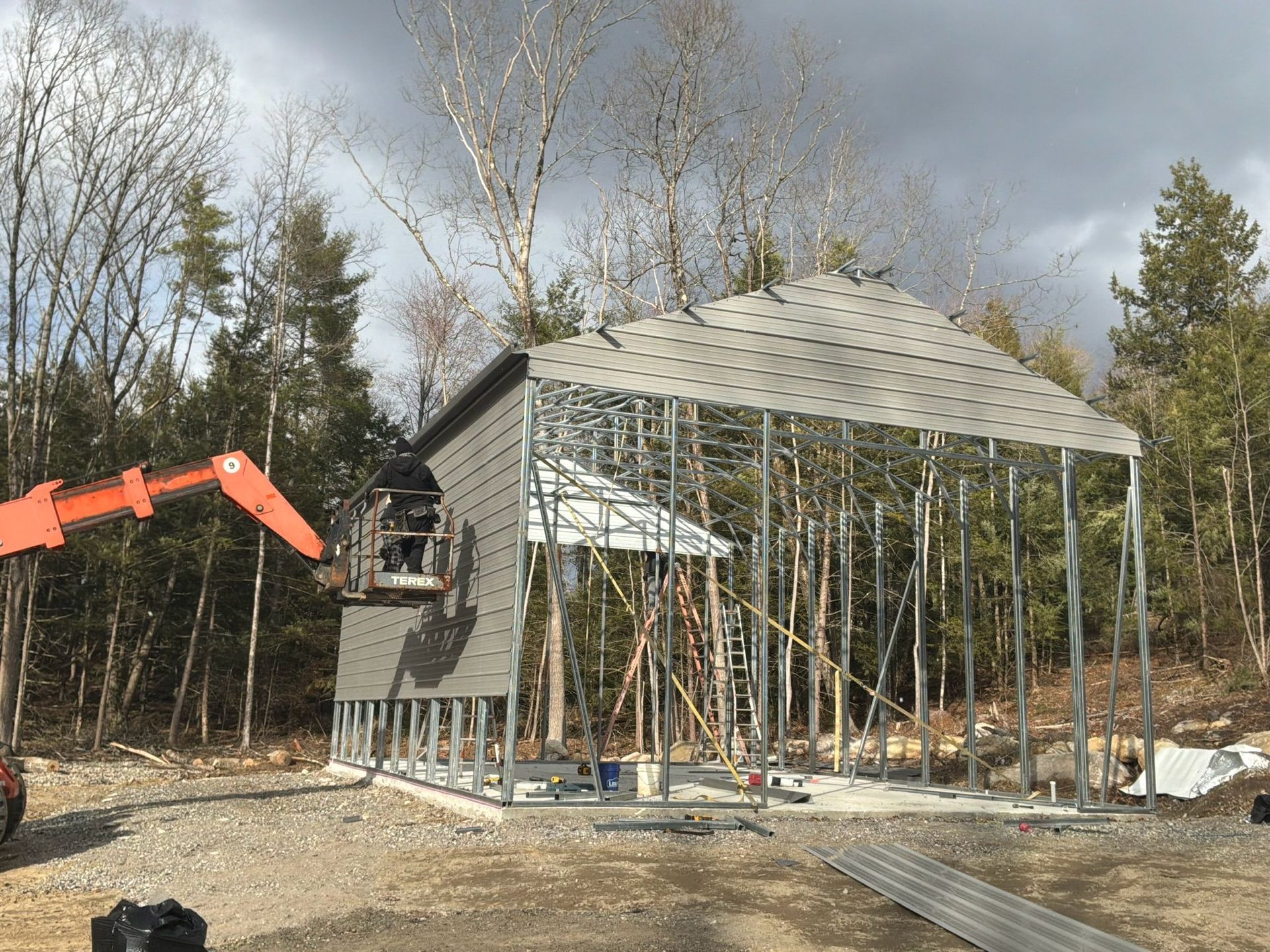 Partially framed small house under construction with exposed roof trusses and a red excavator nearby