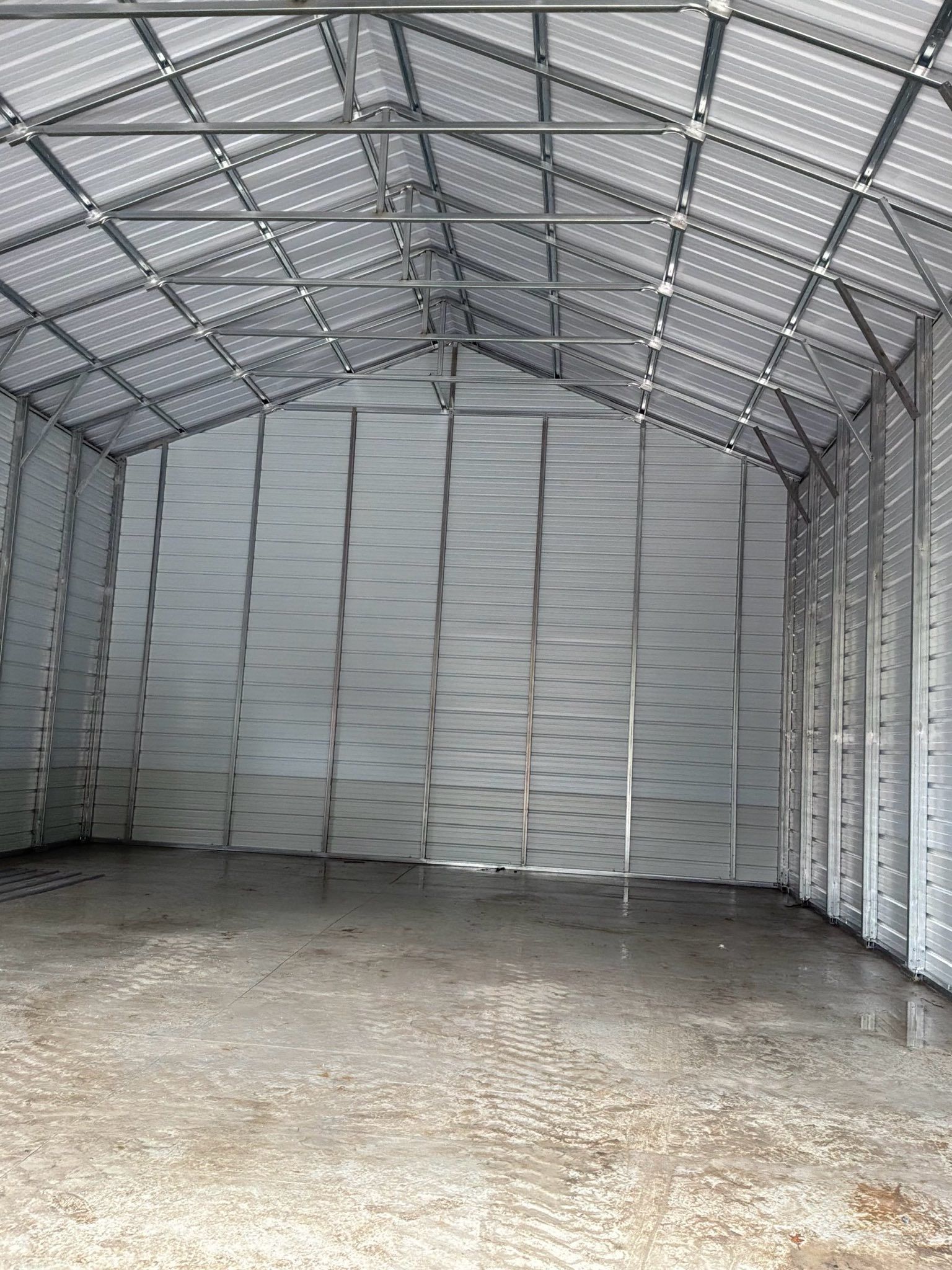 Empty metal shed interior with corrugated walls, mesh roof, and concrete floor