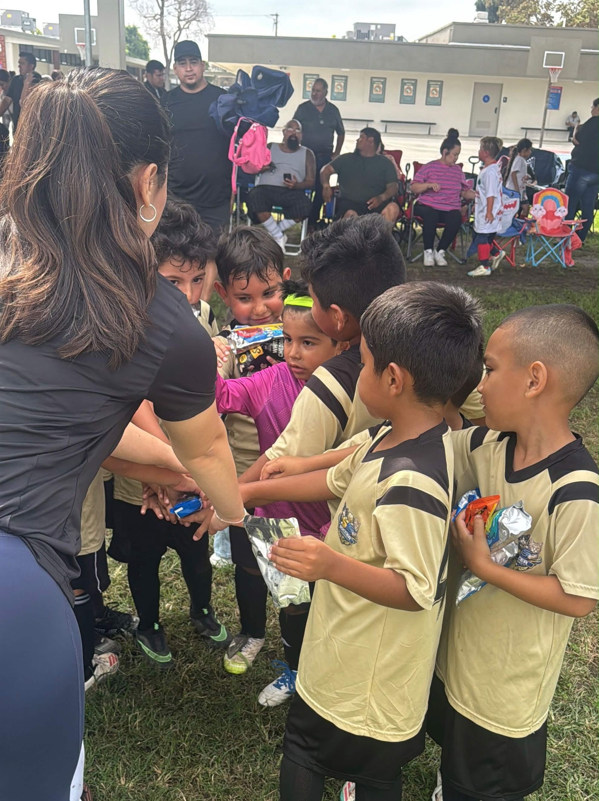 Two children in sports jerseys stand under a roof, facing a field and adjusting their collars.