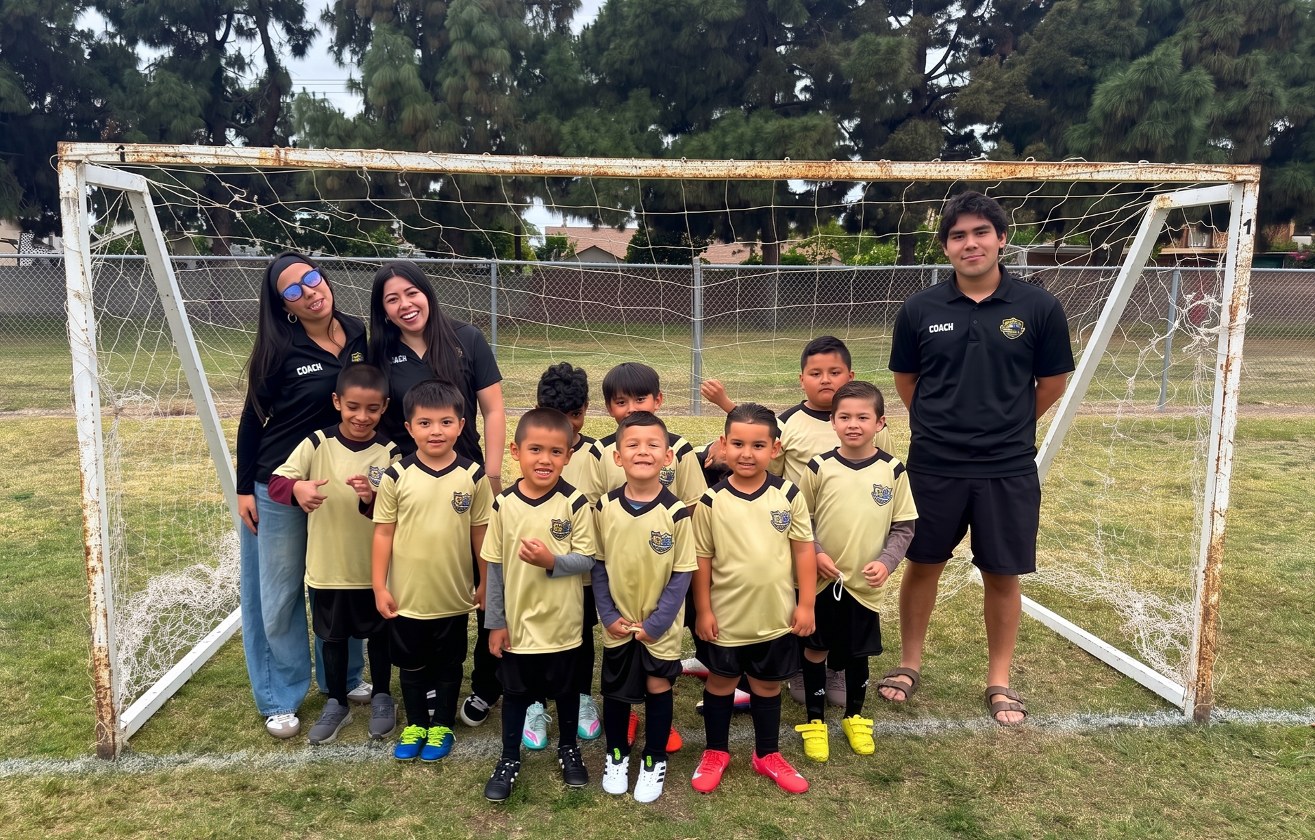 Youth soccer team posing in front of a goal, with two coaches on the ends and trees in the background.