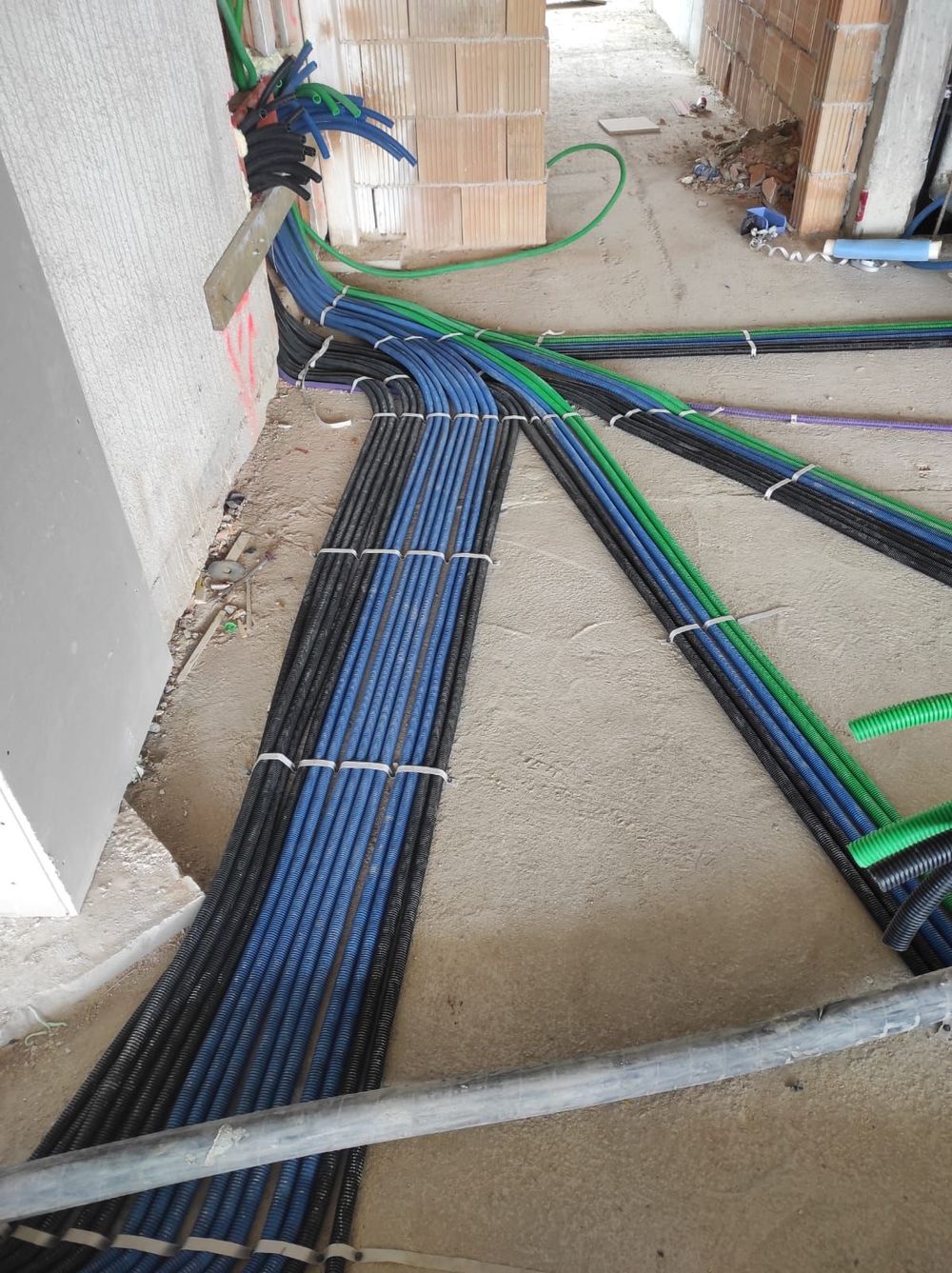 Fasci di tubi blu, neri e verdi sul pavimento di un cantiere edile, fissati con fascette bianche.