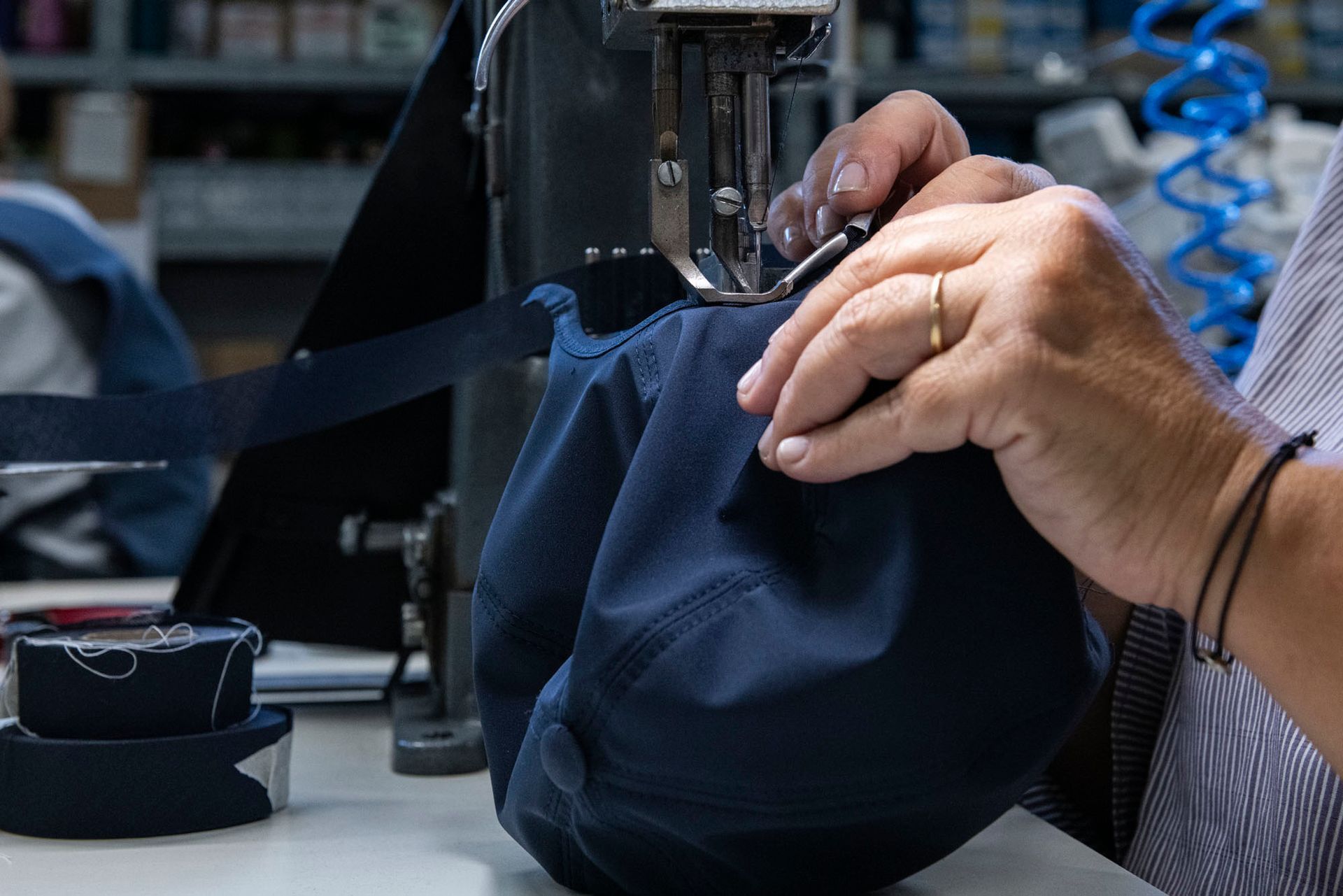 Mani che cuciono una borsa di stoffa blu navy con una macchina da cucire in un laboratorio