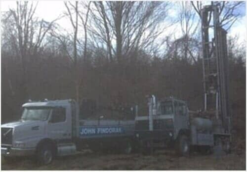 Truck with drilling rig and equipment in a wooded area at dusk