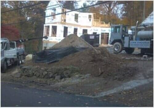 Construction site with dirt piles, parked trucks, and a white building in the background