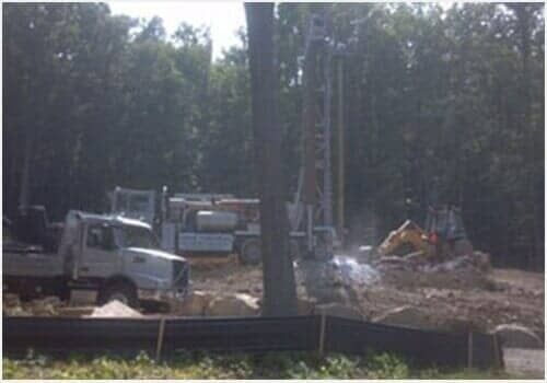 Construction site with trucks and equipment behind a tree line