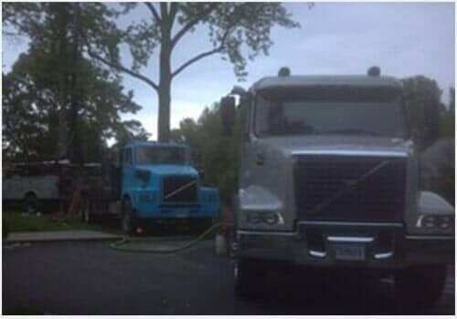 Parked trucks in a lot, including a blue cab and a silver semi, with trees in the background