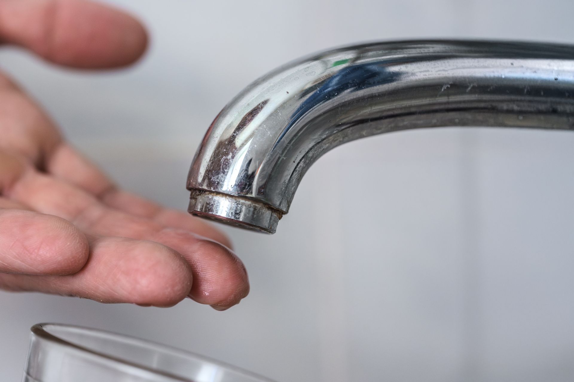 Hand under a chrome faucet catching running water in a sink