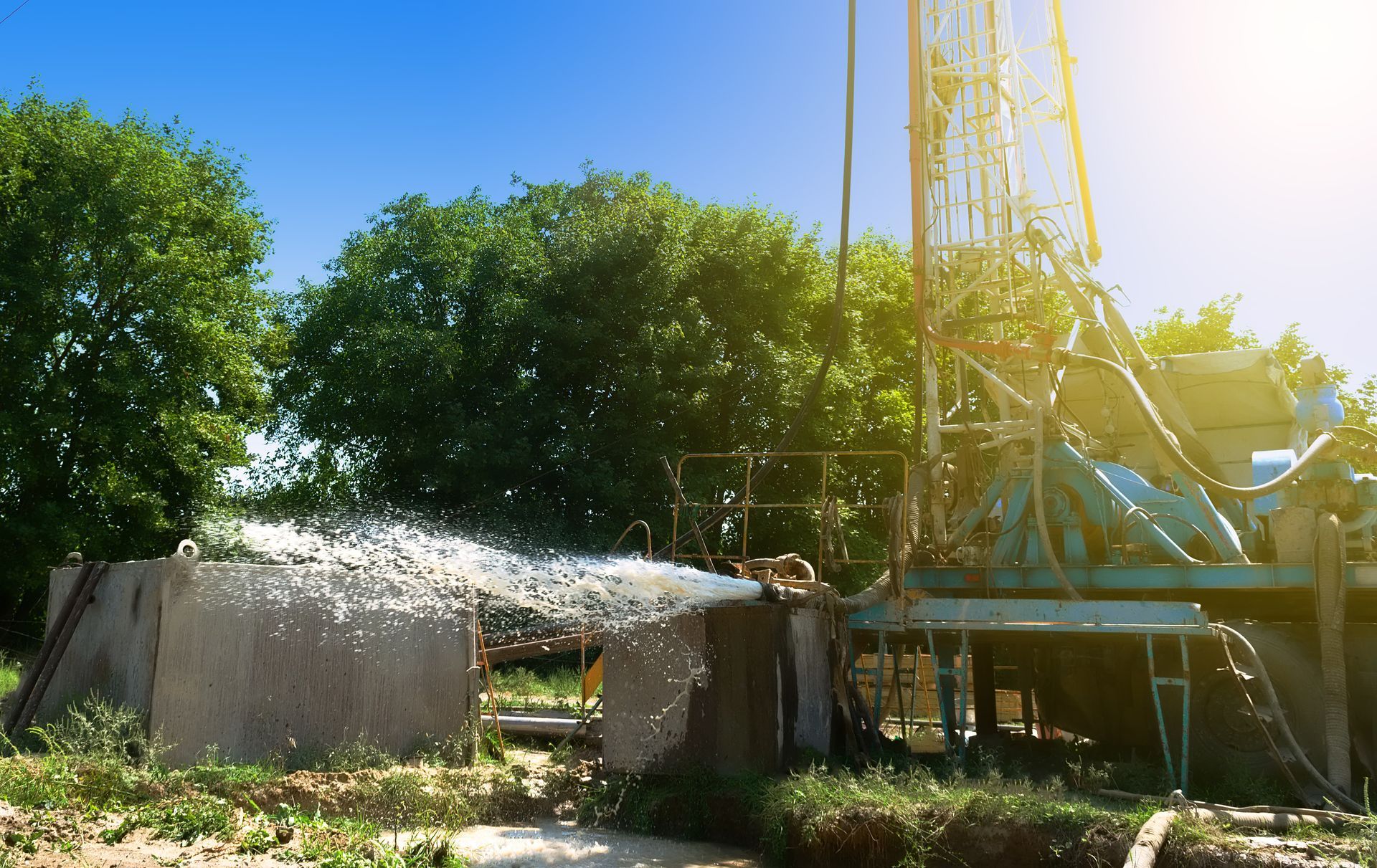 Water spraying from a pipe beside a metal tower and shed in a sunny green field