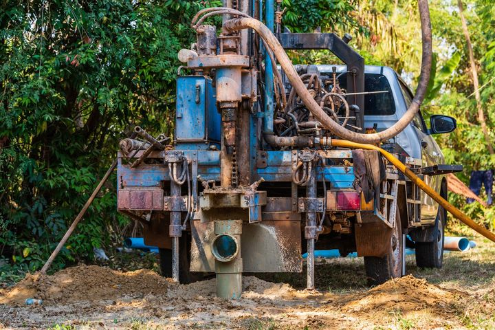 Drilling rig mounted on a truck at a muddy worksite beside a wooded area