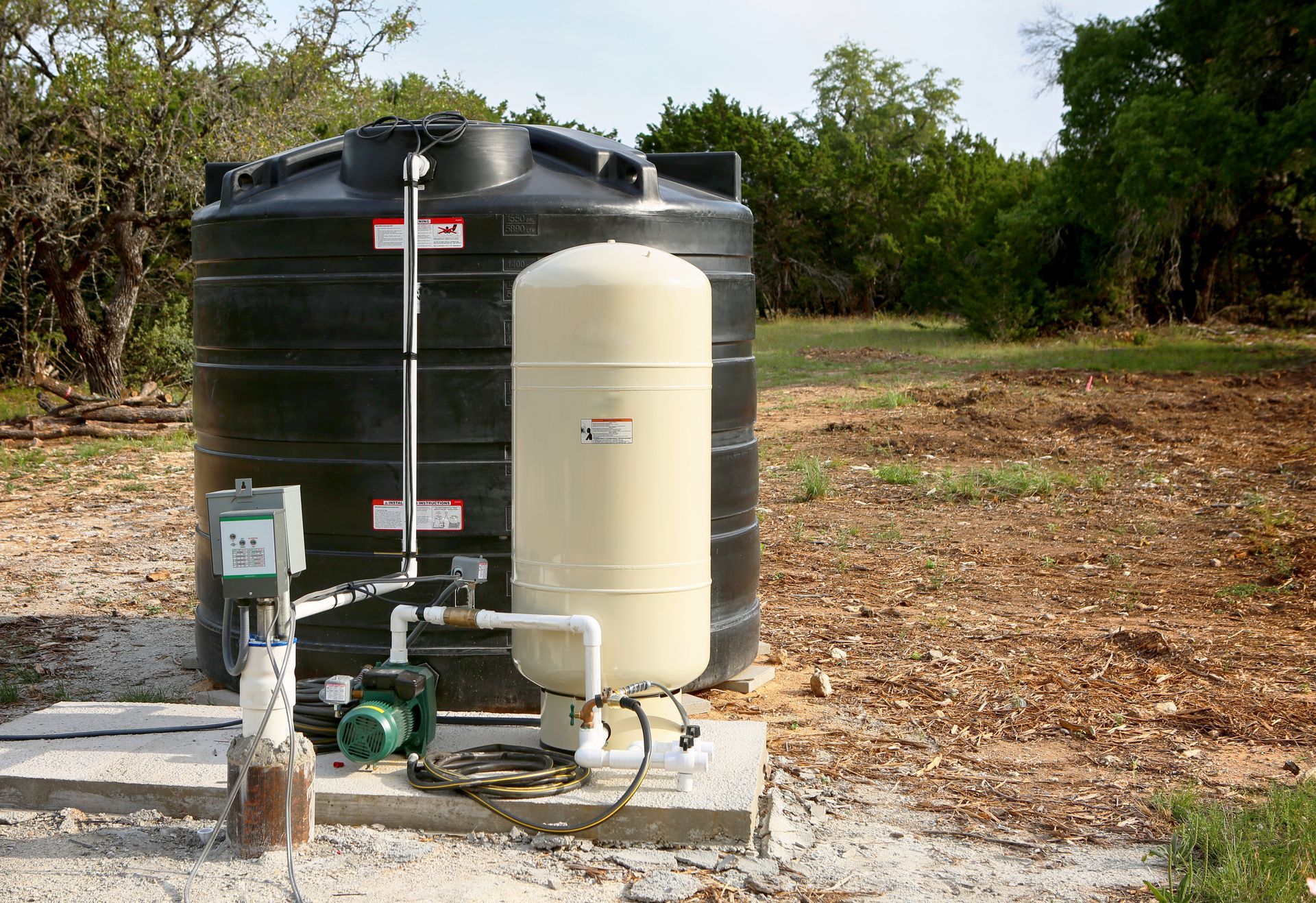 Water filtration tanks and pump equipment beside a large black storage tank outdoors in a rural area