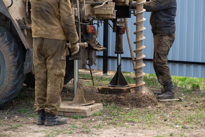 Workers operating a muddy drilling rig beside a blue building