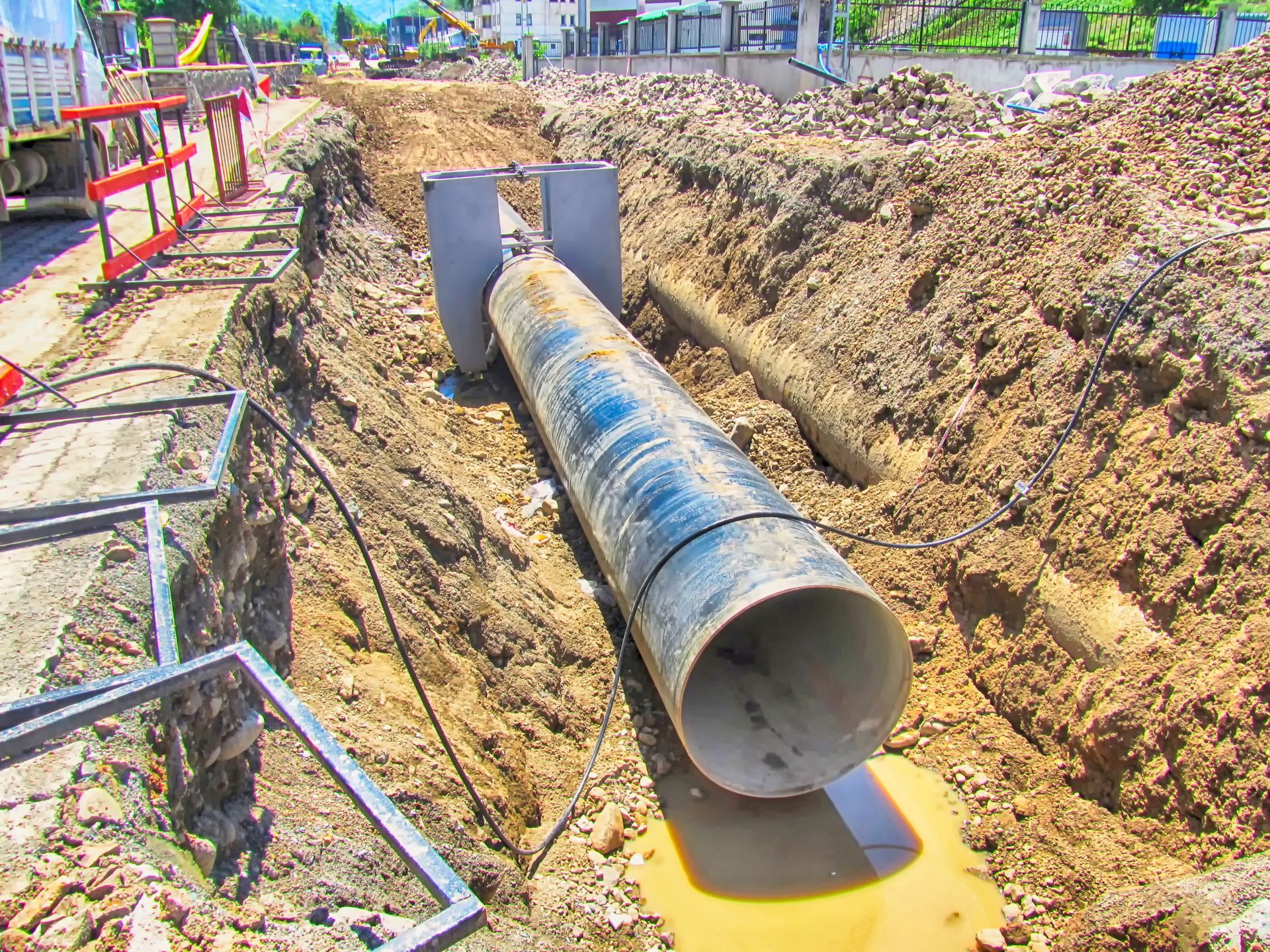 Large metal pipe being laid in an excavation trench at a construction site
