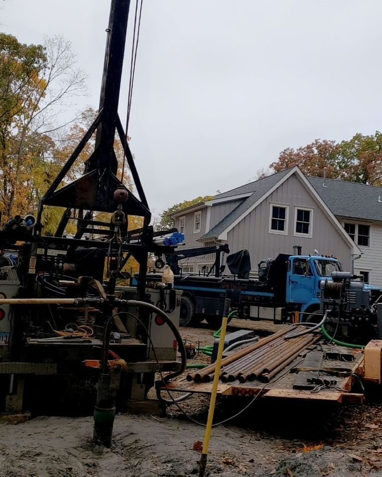 Heavy equipment and flatbed trailer at a worksite beside a gray house in autumn.