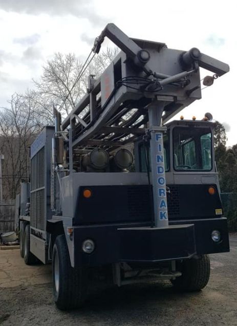 Industrial drilling rig truck with extended boom parked outdoors on a cloudy day