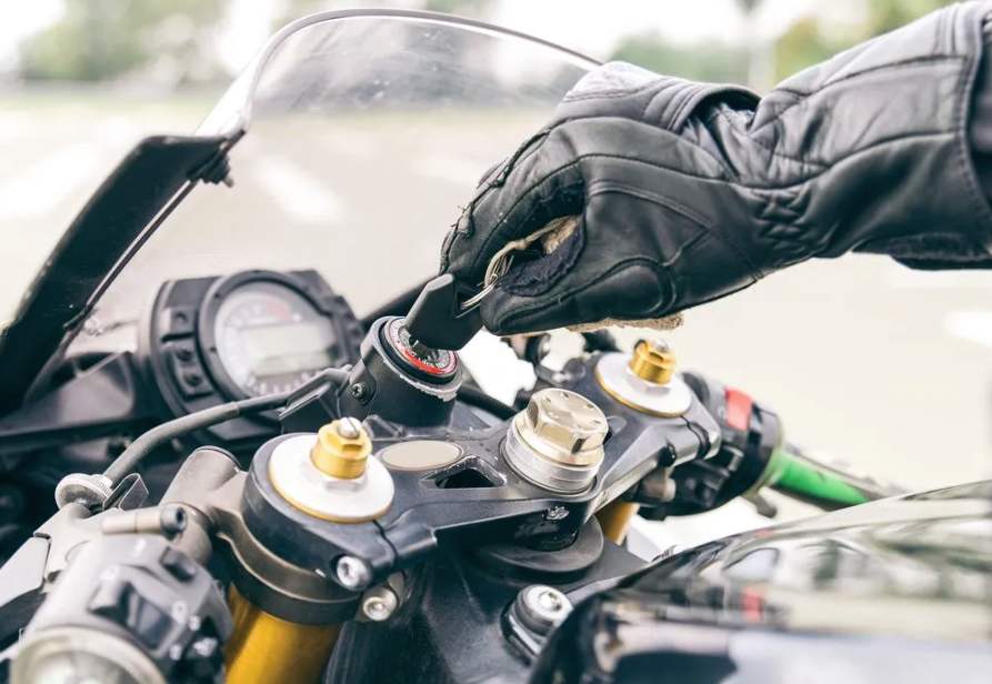 Close-up of a motorbike ignition being turned by a rider wearing black leather gloves