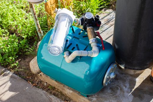 Outdoor irrigation valve box with pipes, a pressure gauge, and a black pipe beside a garden bed