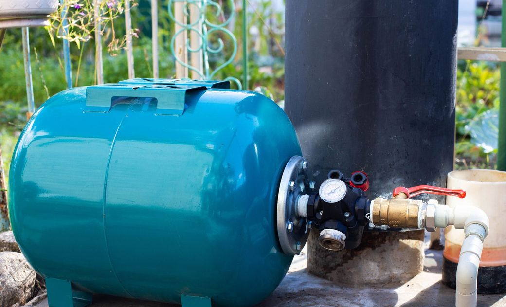 Blue water pressure tank with pipe valves outdoors near a wall