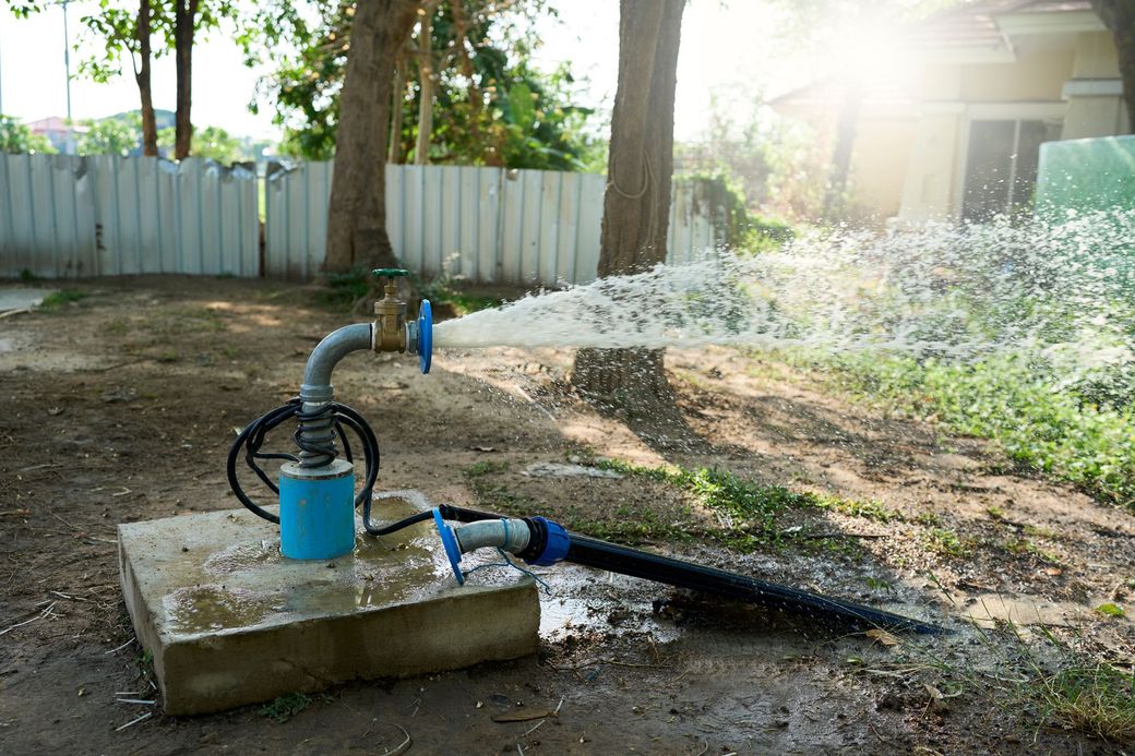 Blue water pump spraying water onto a lawn in a sunny yard with a fence and trees behind it