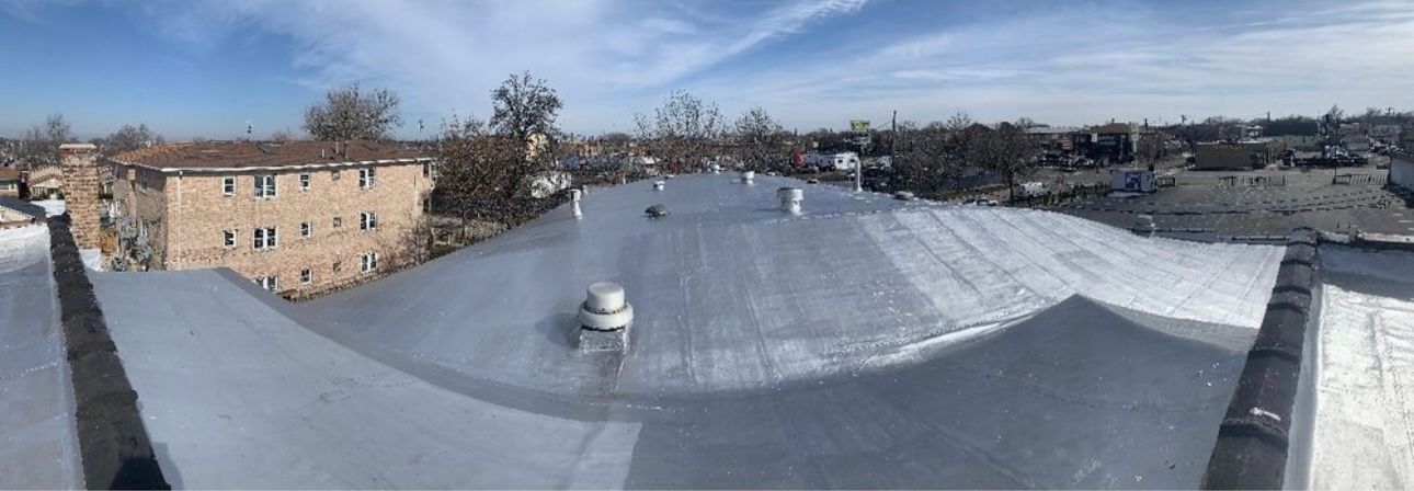 A wide-angle view of a flat roof covered in snow with several ventilation pipes. A building is visible in the distance.