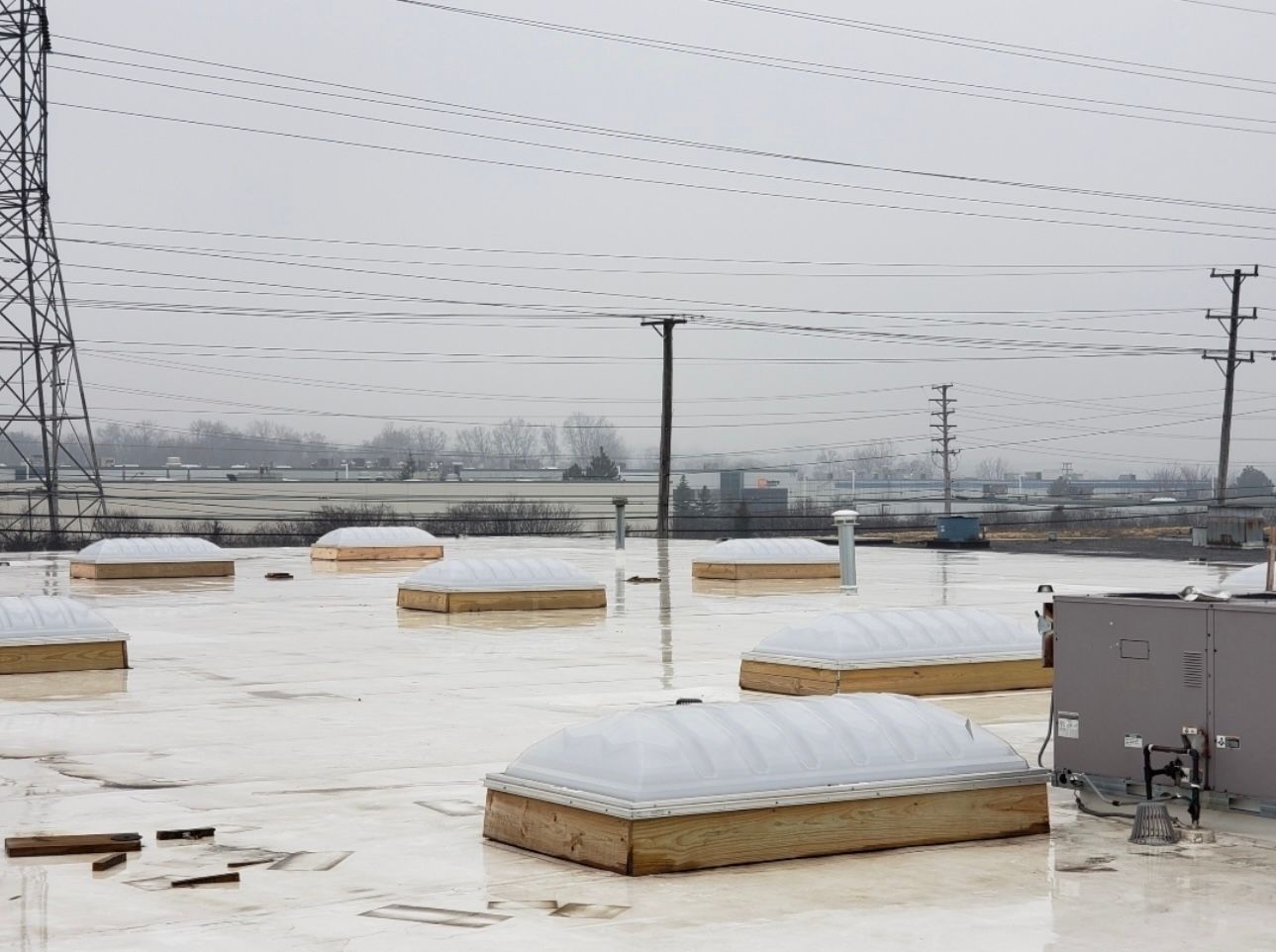 A snowy rooftop with several dome-shaped skylights. Power lines and utility poles fill the background.