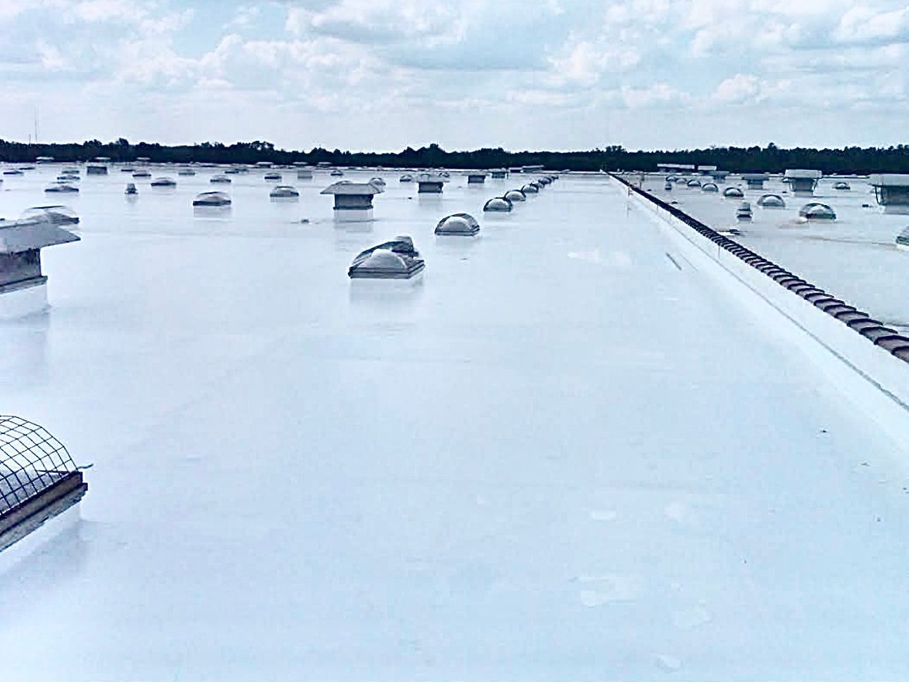 A large, white commercial roof with many vents, under a partly cloudy sky.