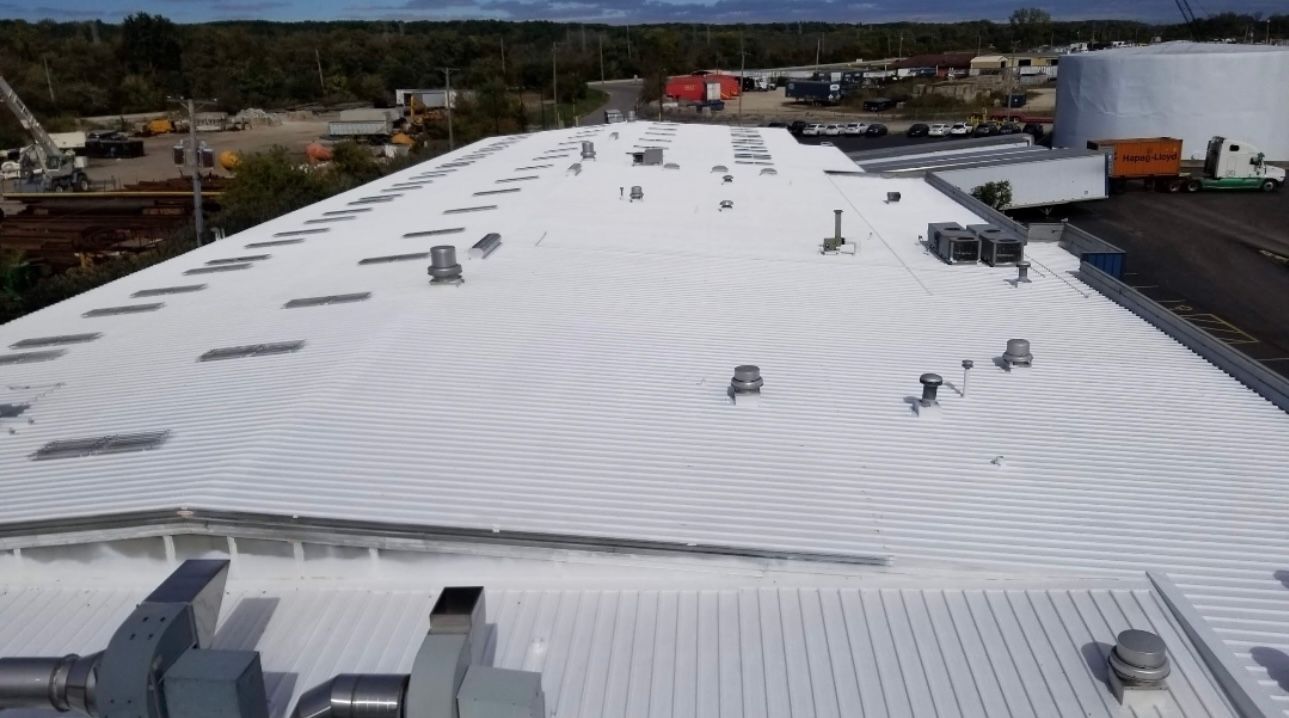 White commercial roof with multiple vents and HVAC units, outdoors with buildings and sky in the background.