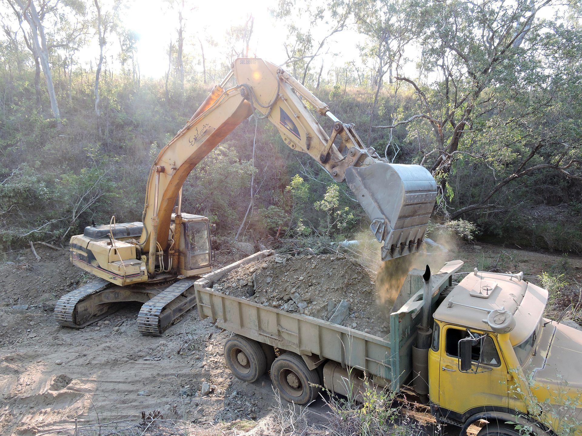 An excavator loading sand from a creek into a dump truck to extract the alluvial gold