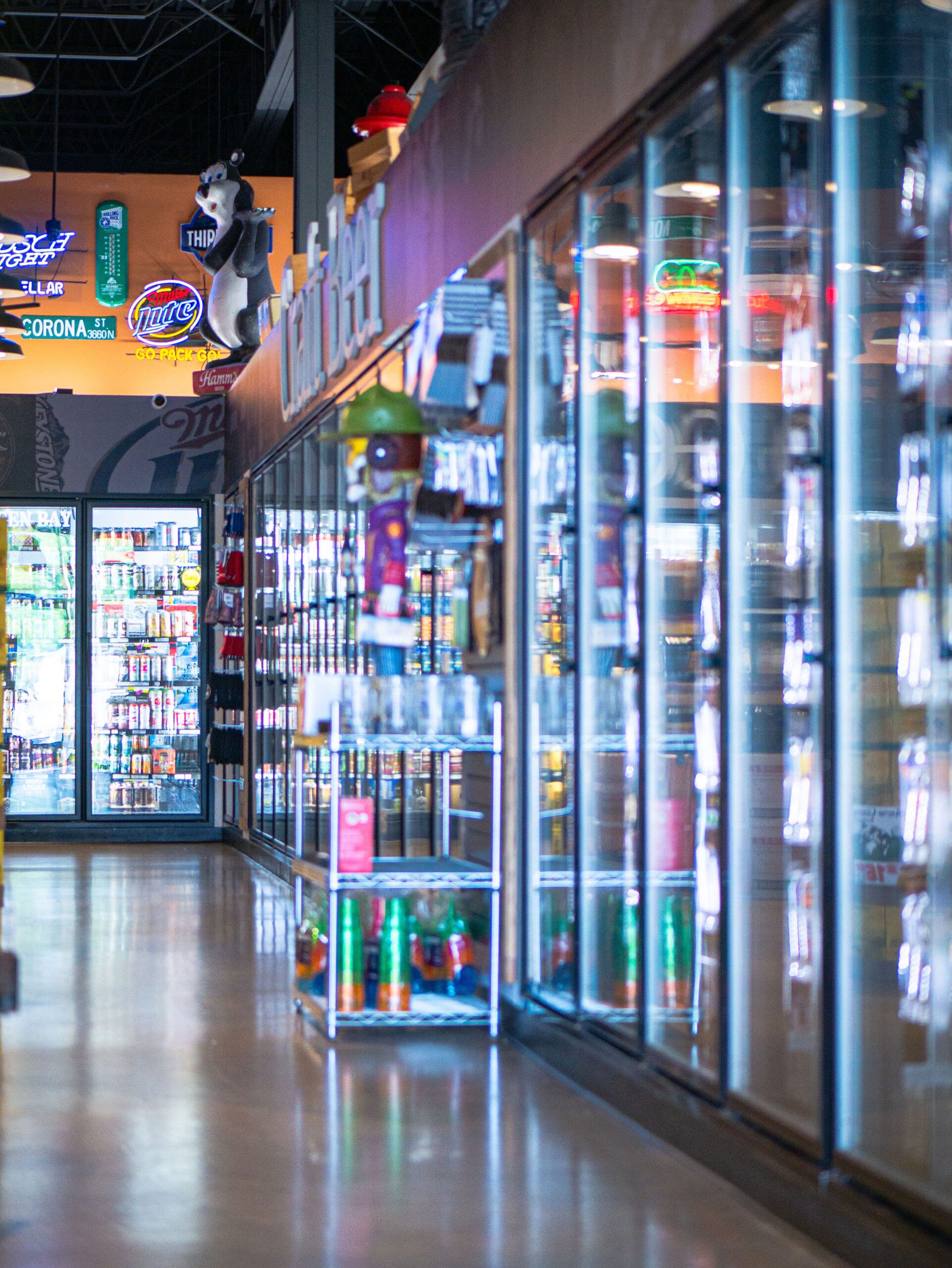 A convenience store aisle with glass-door refrigerators and colorful drinks lining the right side.
