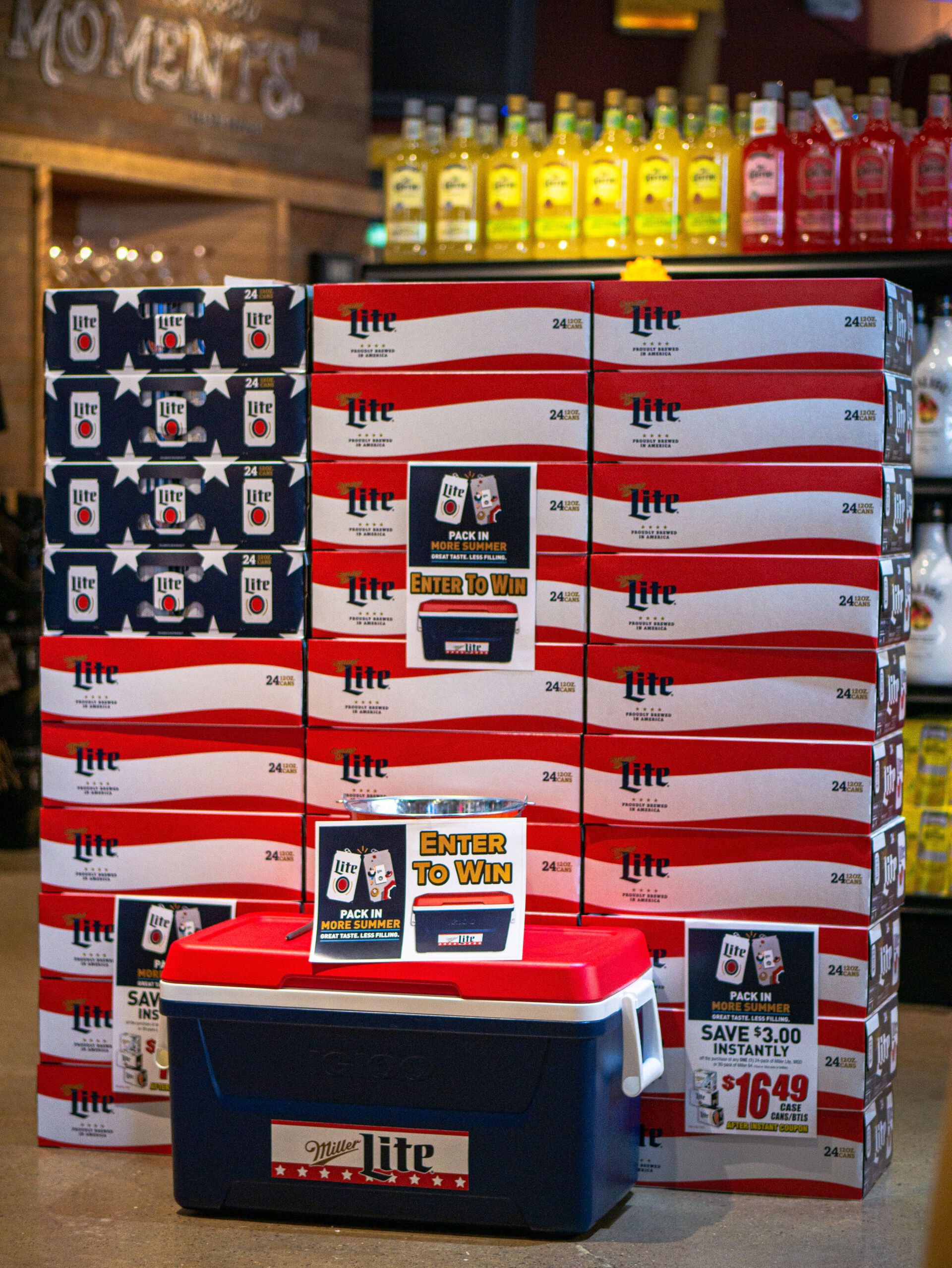 Stacks of Miller Lite beer boxes and cases arranged beside a cooler with bottles on top.