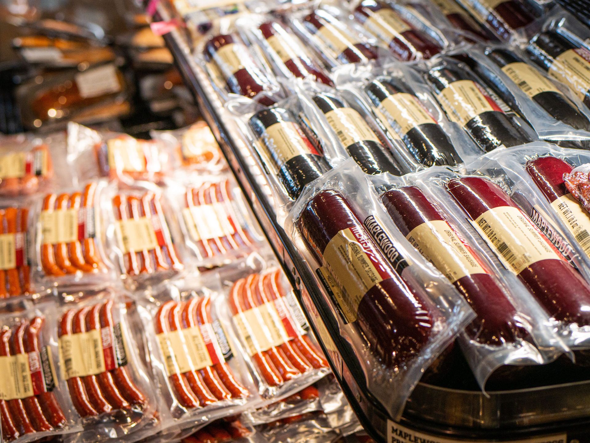 Packed grocery display of assorted vacuum-sealed meats and sausages in clear plastic trays.