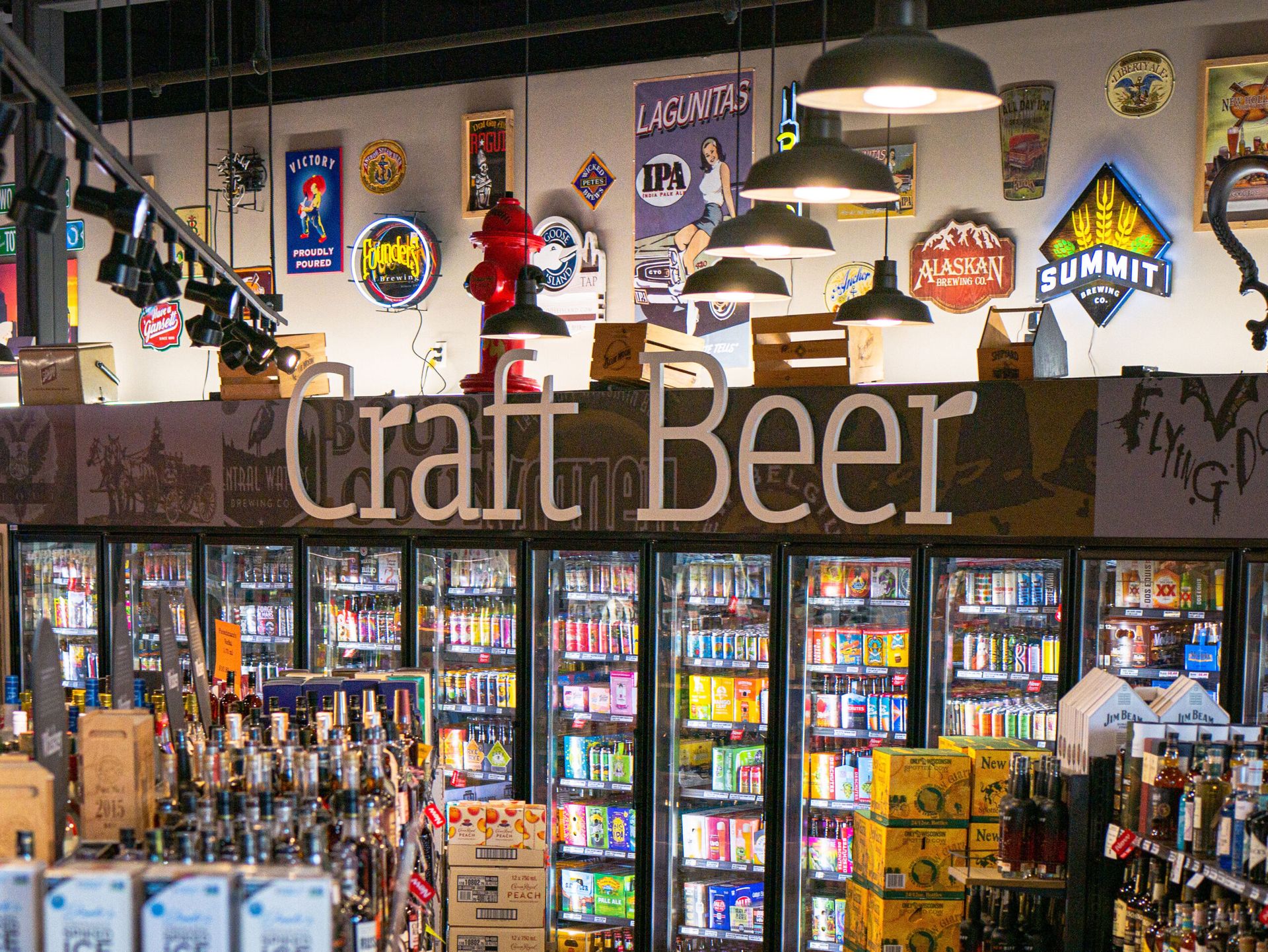 Craft beer display in a bar, with refrigerators, bottles, and brewery signs on the wall.