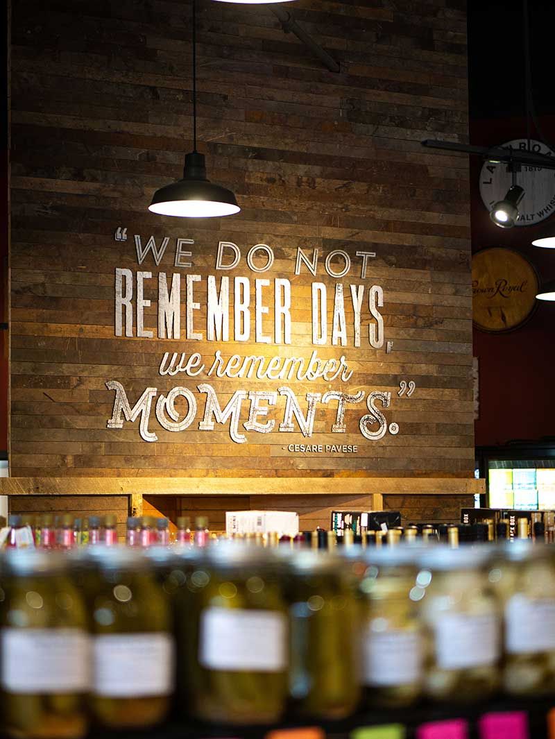 Bar wall with a wooden sign reading “We do not remember days, we remember moments” above blurred wine bottles