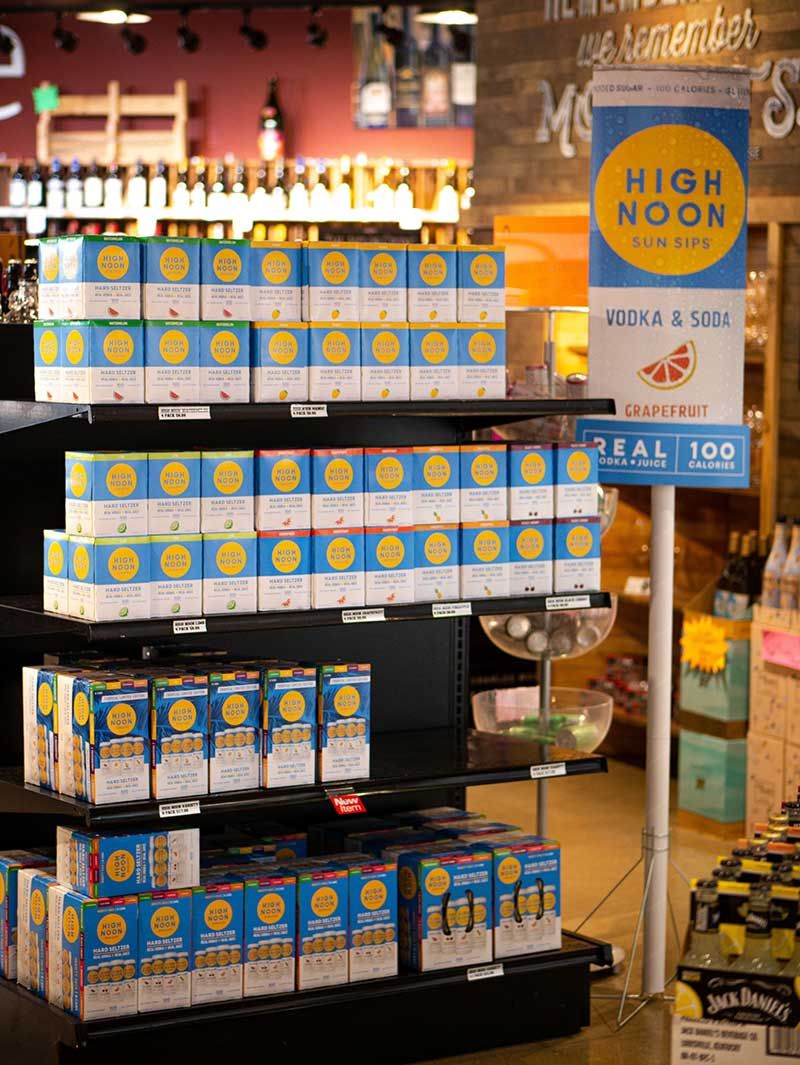 Display of High Noon hard seltzer packs on black shelves in a store aisle