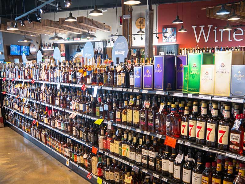 Wine store aisle with rows of liquor bottles and colorful wine displays under hanging lights