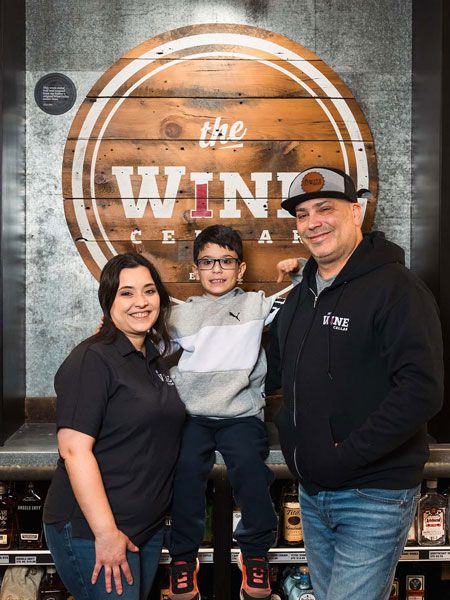 Three people smiling in front of a large “The Wing” sign indoors