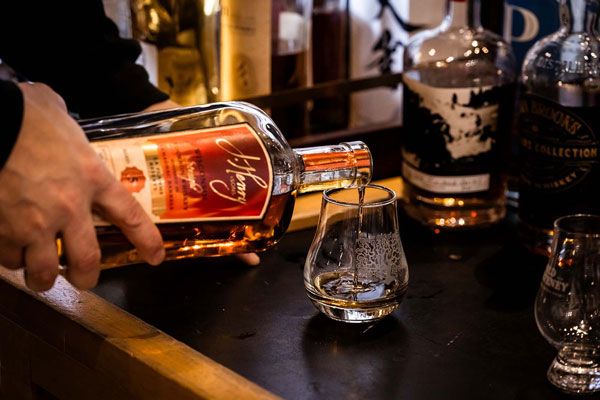 Hand pouring amber whiskey into a glass on a bar counter